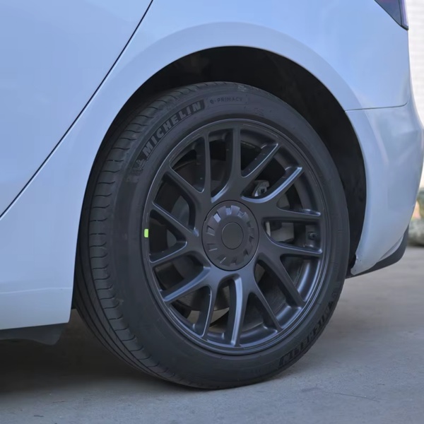 Detailansicht der sportlichen grauen Nabenkappe auf der dunklen Felge eines Tesla Model 3 Highland (2024).