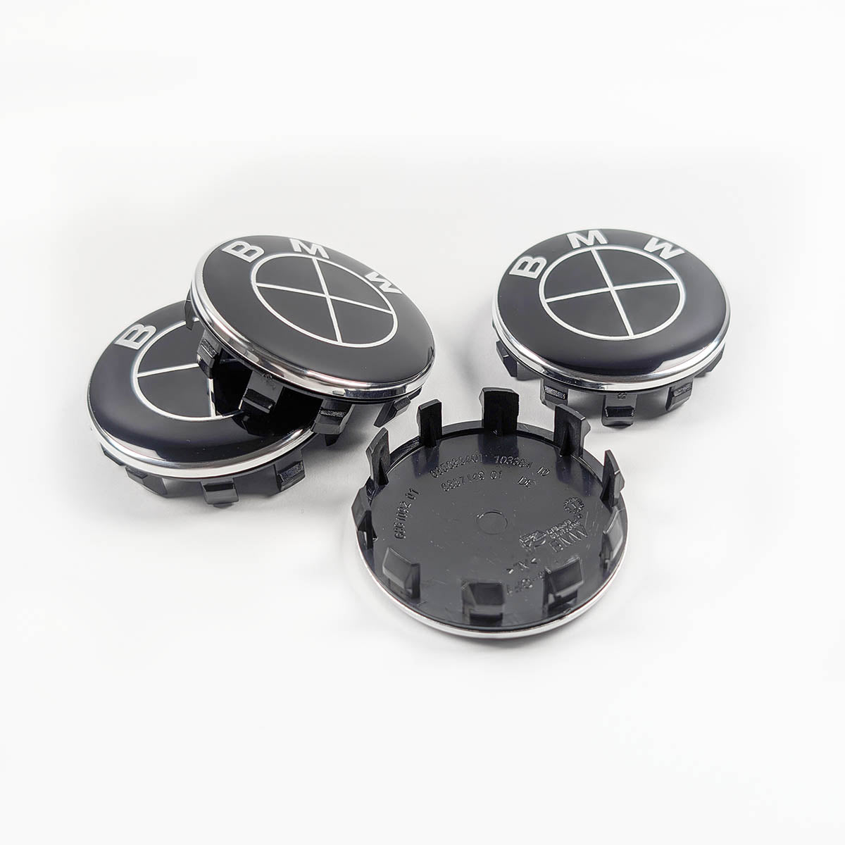 Vierer-Set BMW Radnabenabdeckungen (56mm). Drei Kappen sind arrangiert und zeigen das schwarz-weiße BMW-Emblem, eine Kappe liegt daneben auf der Rückseite und zeigt die Kunststoff-Clips