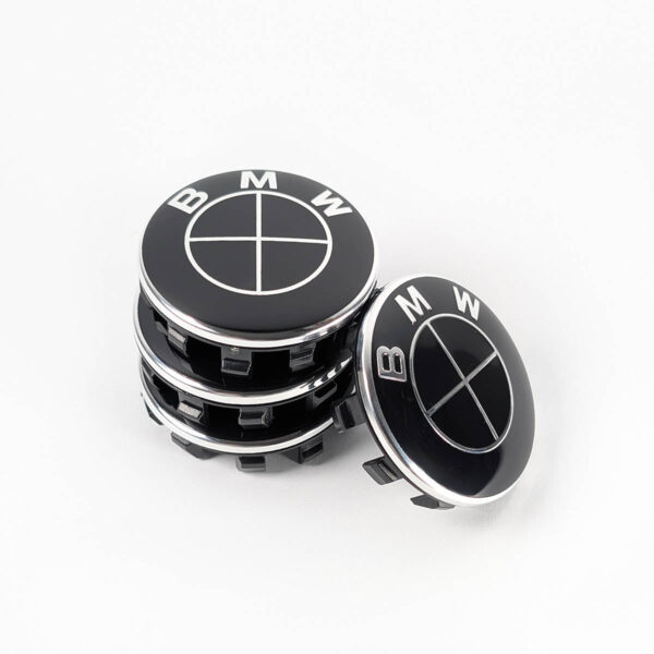 Gestapeltes Set von schwarzen BMW Nabendeckeln. Drei Kappen bilden einen Turm, der die seitliche Struktur und die Clips zeigt, eine vierte Kappe lehnt davor mit Blick auf das Emblem.