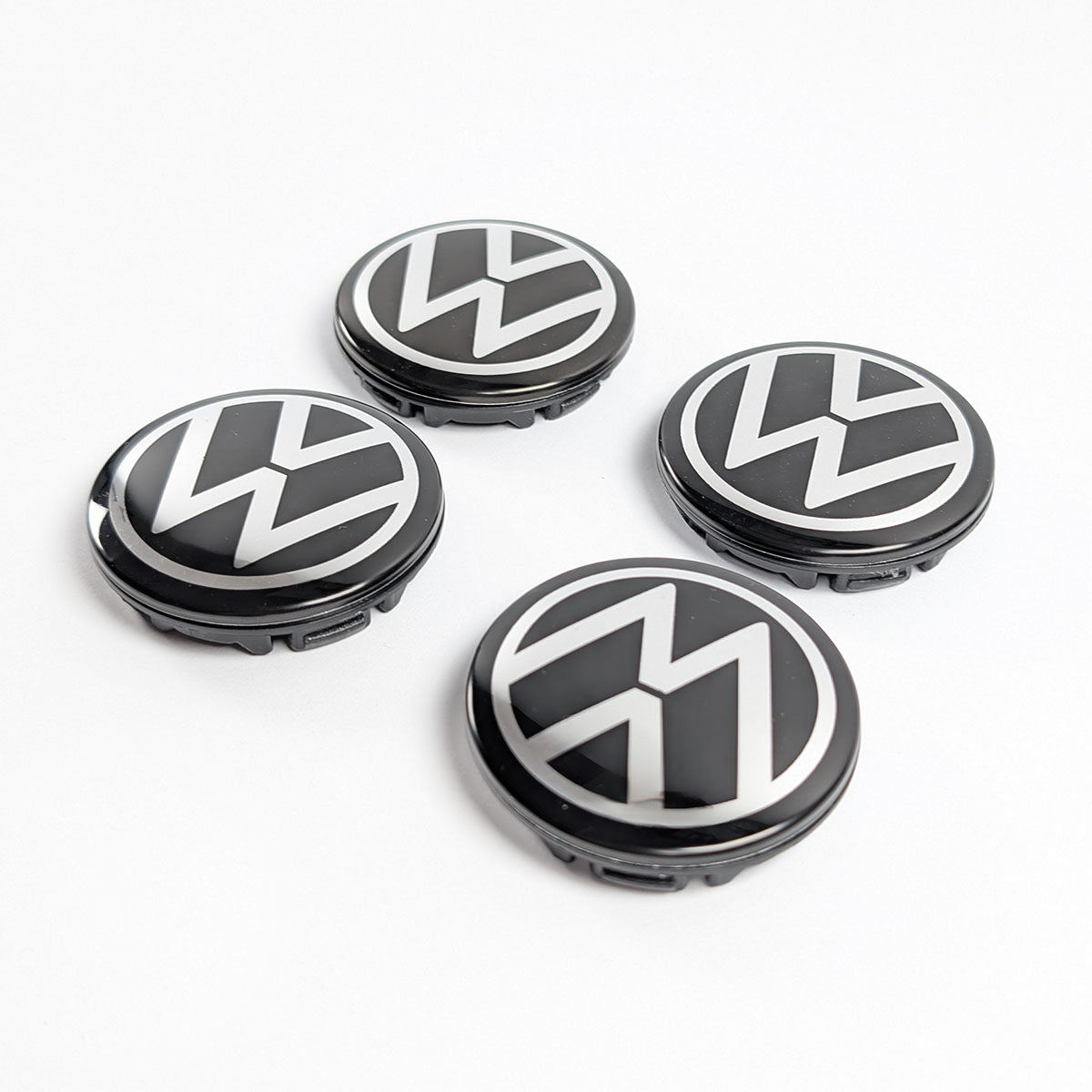 Satz von vier neuen, glänzenden schwarzen Volkswagen Radnabenabdeckungen mit silbernem VW Logo in Frontansicht.
